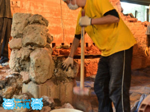 入口の石組み琉球石灰岩をハンマーをで解体する陶工
